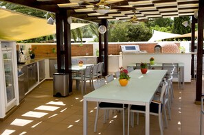 Un área de cocina al aire libre con un horno de ladrillo, una mesa de comedor con sillas y un reloj en la pared.