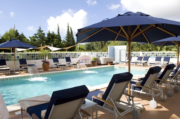 Un área junto a la piscina con sillones de descanso y sombrillas.