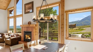 A cozy room with a fireplace, wooden furniture, and large windows offering a view of the outdoors.