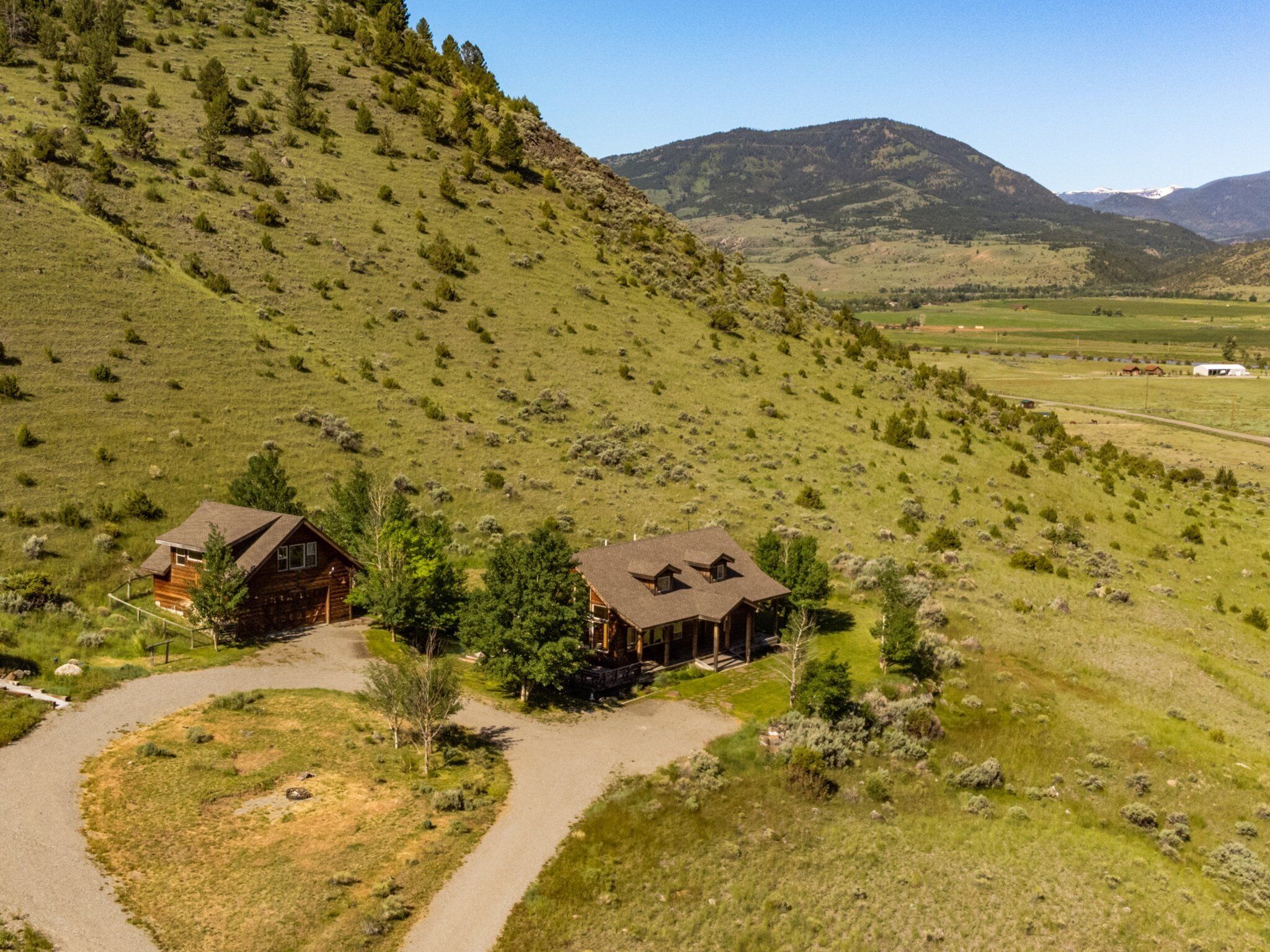 A remote cabin with a dirt path leading to it, surrounded by a hilly landscape and a distant mountain range.