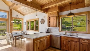 A modern kitchen with wooden cabinets, a central island, and large windows offering a view of the outdoors.