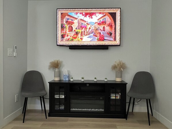 A living room with a flat-screen TV mounted on the wall, a black entertainment unit below, two grey chairs, and a vase with dried plants. - Private/Relaxing New Guest House & Fast Wi-Fi (Pittsburg)