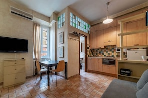 A compact living space with a dining area, kitchenette, and a TV mounted on the wall.
