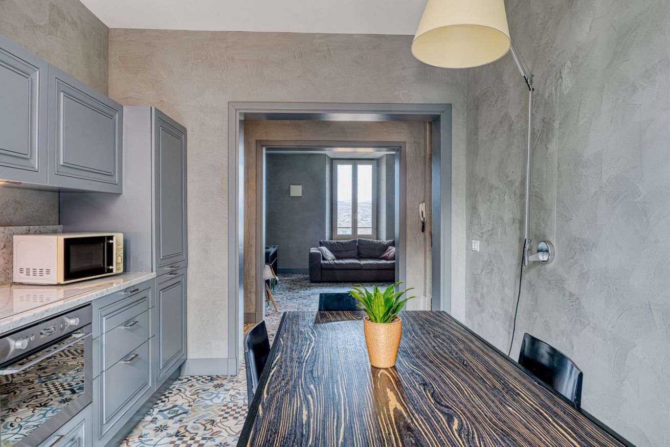 A modern kitchen with grey cabinets, a microwave, and a dining table with a plant.