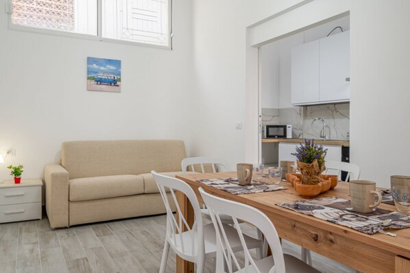 A modern kitchen with white cabinets, a wooden dining table, and a beige sofa.