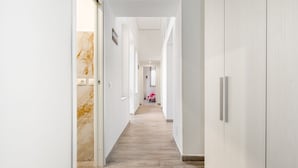 En modern hall med en vägg av marmor, ett trägolv och utsikt in i ett rum med en säng.