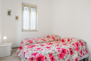 A bedroom with a bed, a nightstand, a window with curtains, and two wall decorations.