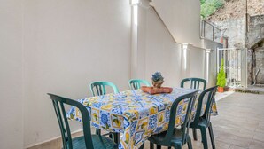 En täckt uteplats med ett bord och stolar, en krukväxt och utsikt över en bergig sluttning.