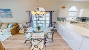 A modern kitchen with a glass dining table, white cabinetry, and a view of the city through large windows.