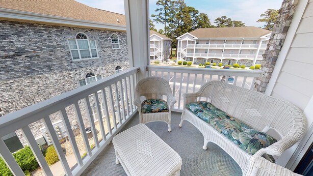 A balcony with wicker furniture, a stone building in the background, and a white building with balconies.