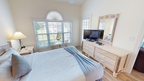 Une chambre à coucher comprenant un lit, une commode, un téléviseur et une fenêtre avec des stores.