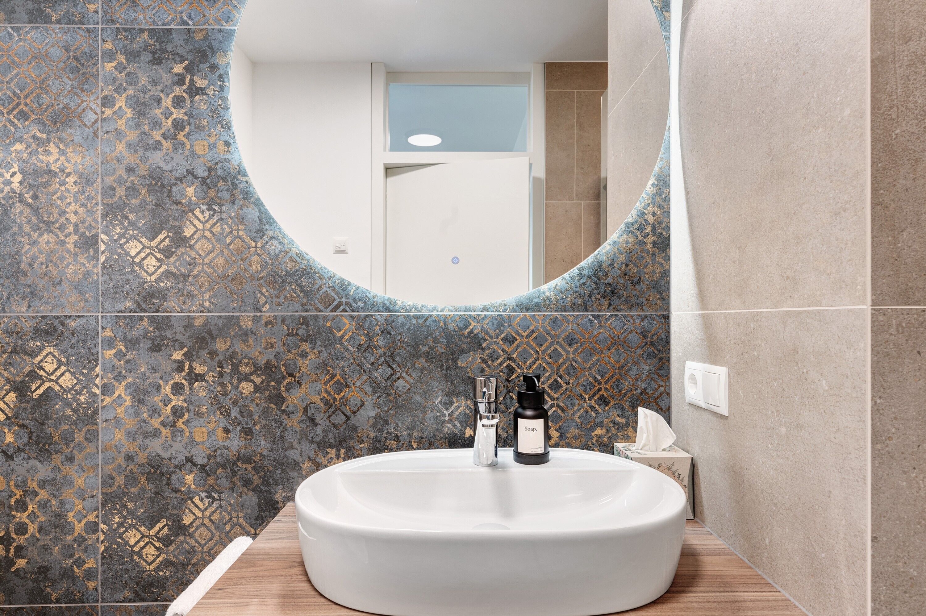 A bathroom with a white sink, a mirror, and patterned tiles.