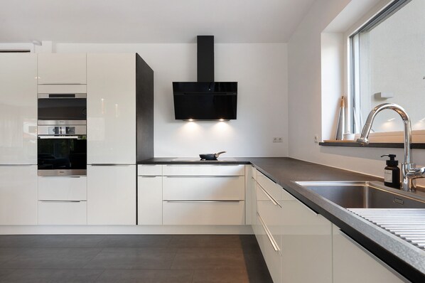A modern kitchen with white cabinetry, a black range hood, and a stainless steel sink. - Apartment 'Vinea Guesthouse Garden' with Mountain View, Wi-Fi and Air Conditioning (Cornedo All'isarco)
