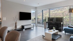 Una sala de estar moderna con un televisor de pantalla plana, un piano y un gran ventanal con vistas a un paisaje montañoso.