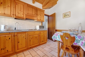 Una cocina con armarios de madera, microondas, hervidor y una mesa de comedor con sillas.