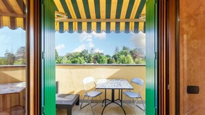 A balcony with a table and chairs, a bench, and a view of trees and hills.