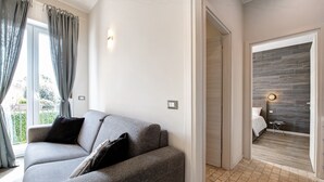 A modern room with a grey sofa, a small table, and a bed with a dark wood headboard. - Apartment 'Garda Flow' with Wi-Fi and Air Conditioning (Lonato del Garda)