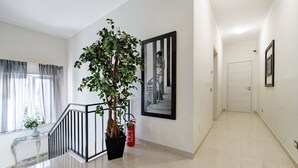 A hallway with a staircase, a potted plant, a fire extinguisher, and framed pictures on the walls. - Apartment 'Garda Flow' with Wi-Fi and Air Conditioning (Lonato del Garda)