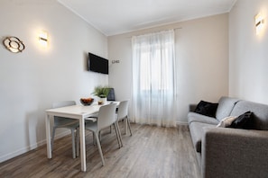 A modern living room with a dining table, chairs, a grey sofa, and a TV mounted on the wall. - Apartment 'Garda Flow' with Wi-Fi and Air Conditioning (Lonato del Garda)