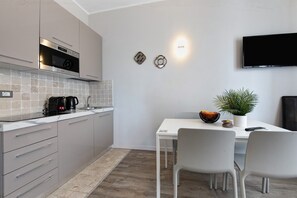 A modern kitchen with a built-in oven, a coffee maker, and a dining area with two chairs and a table. - Apartment 'Garda Flow' with Wi-Fi and Air Conditioning (Lonato del Garda)
