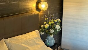 Una habitación de hotel moderna con cabecera de madera, una mesita de noche con un florero y un ventanal grande.