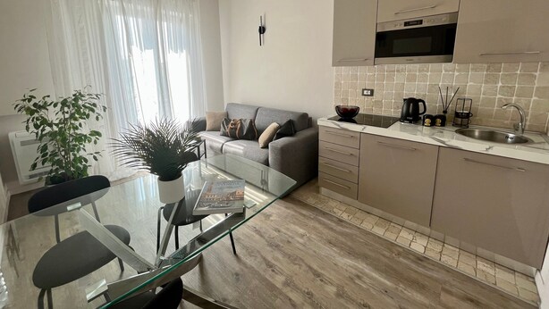 Una cocina moderna con microondas, estufa y lavaplatos. Hay una mesa de vidrio con sillas, un sofá y una planta en maceta.