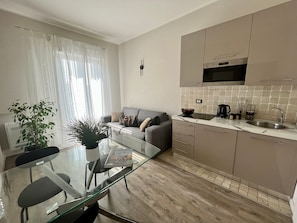 A modern kitchen with a microwave, stove, and sink. There's a glass dining table with chairs, a sofa, and a potted plant. - Apartment 'Garda Flow Bilocale' with Wi-Fi and Air Conditioning (Lonato del Garda)