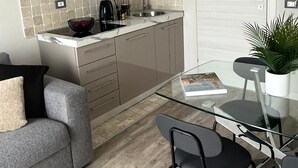 Una cocina compacta con microondas, fregadero y armarios, una mesa de vidrio con sillas, y un sofá gris.