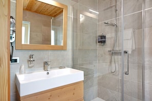 A modern bathroom with a white sink, wooden vanity, a large mirror, and a glass-enclosed shower area.