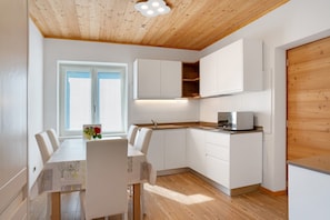 A modern kitchen with white cabinets, a wooden ceiling, and a dining area with a table and chairs.