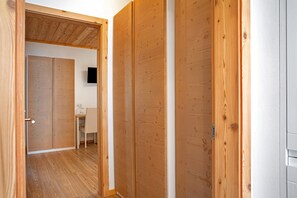 Une porte en bois donne sur une pièce où se trouvent un bureau et une chaise, un téléviseur fixé au mur et un plafond en bois.