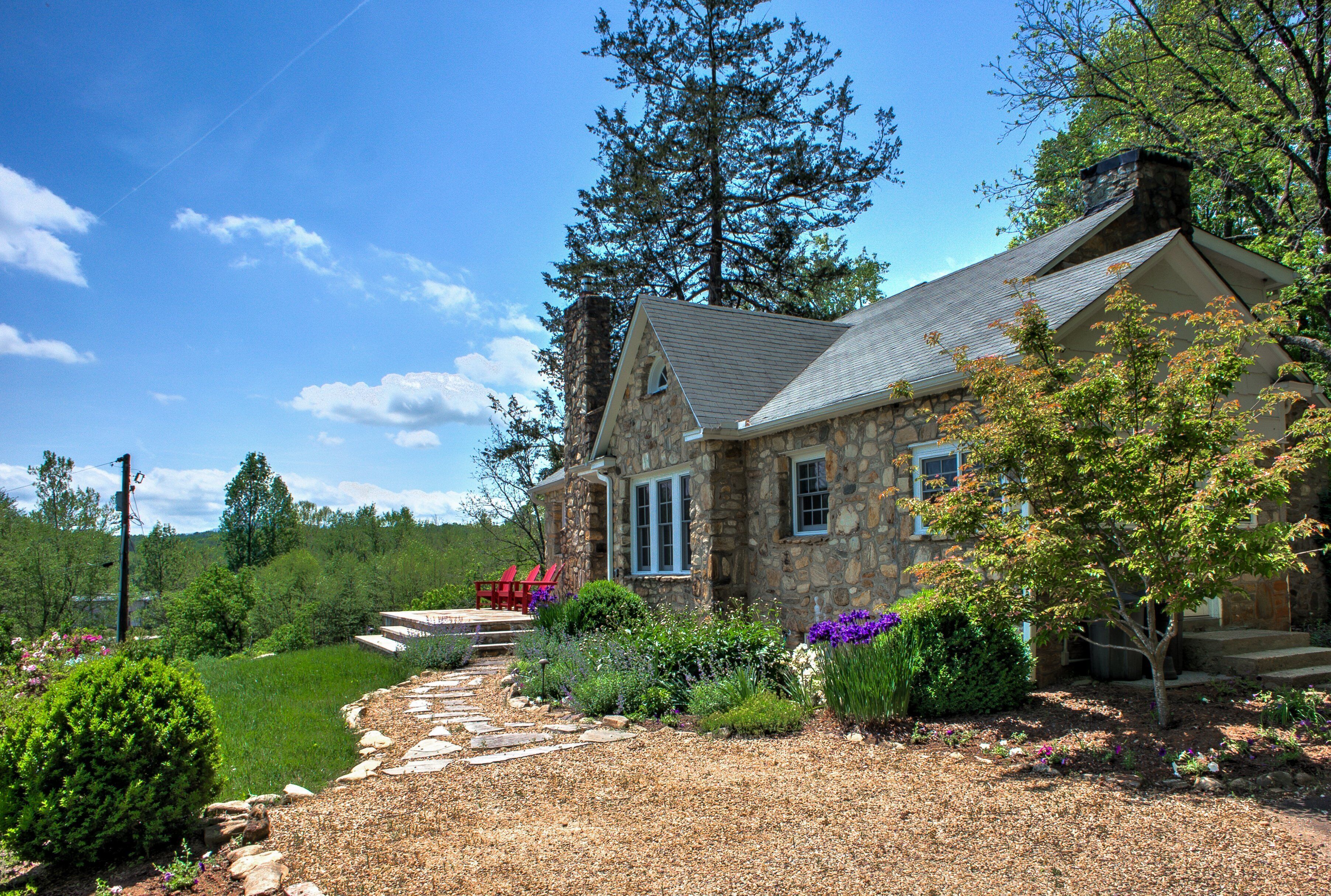 A stone house with a stone chimney, a stone pathway leading to the front door, and a red chair outside.