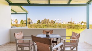 Un área de estar al aire libre con techo, mesa y sillas, y vistas a un paisaje verde con árboles y edificios a lo lejos.