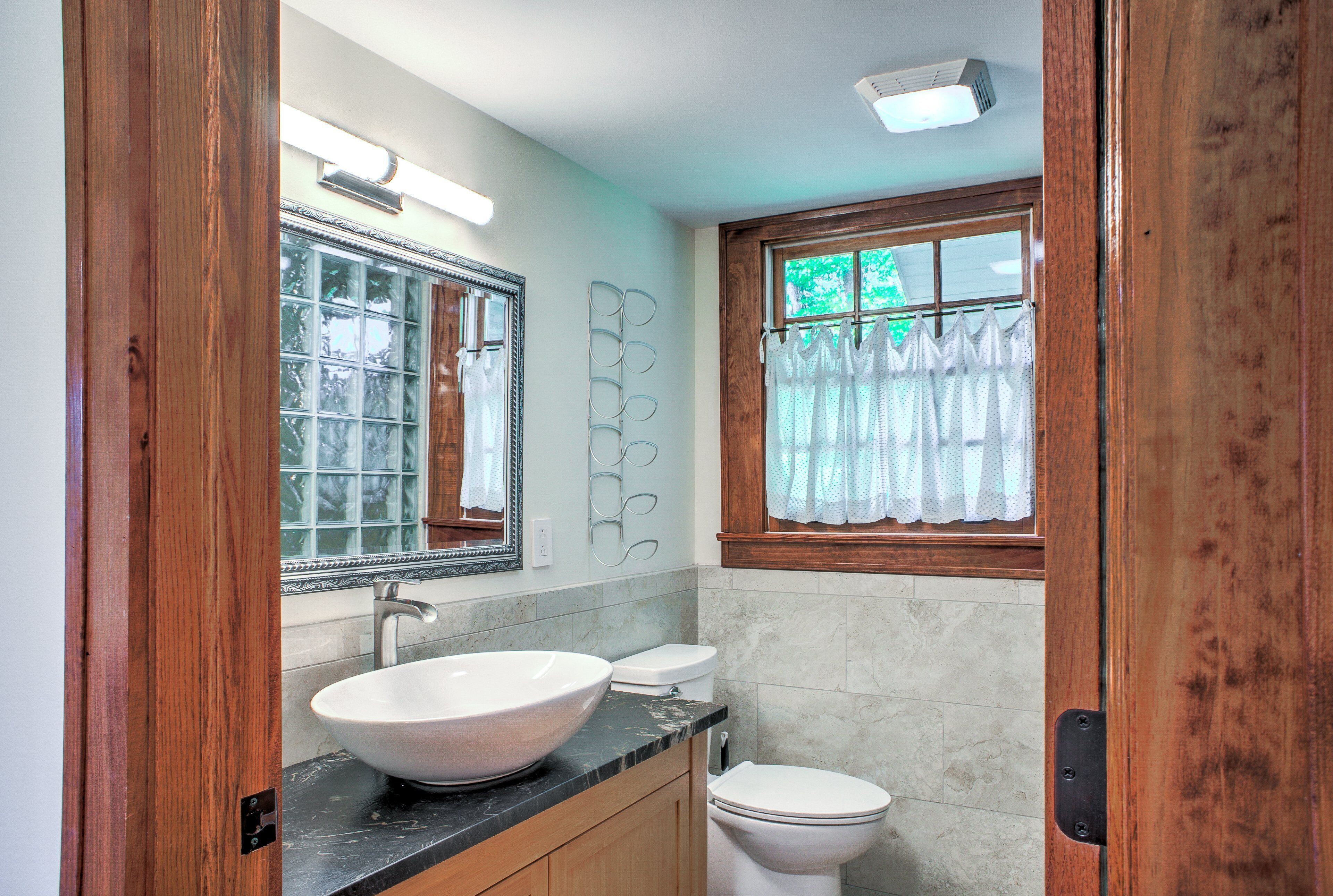 Une salle de bain comprenant un grand lavabo sur pied, des toilettes, un miroir et une fenêtre avec des rideaux.