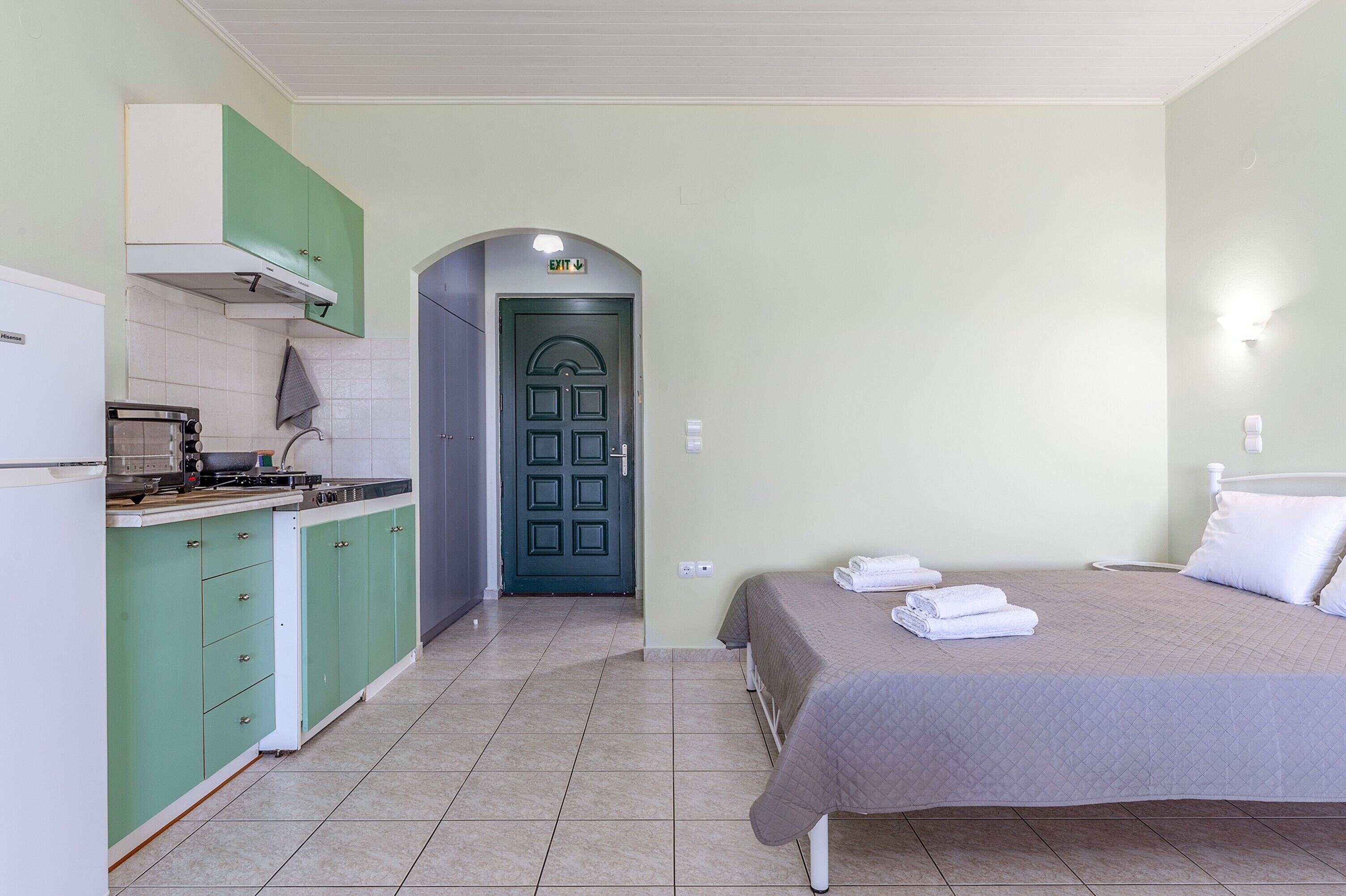 A room with a bed, a kitchenette, and a green door.