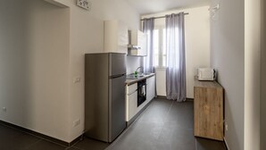 A compact kitchen with a refrigerator, oven, sink, and a microwave on a wooden cabinet.
