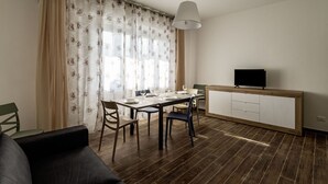 A modern living room with a dining area, a flat-screen TV, and a wooden cabinet.