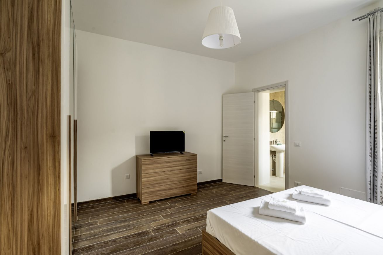 A bedroom with a bed, a dresser, a television, and a bathroom visible through an open door.