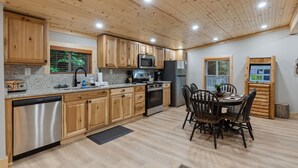 A modern kitchen with wooden cabinets, stainless steel appliances, and a dining area with a wooden table and chairs.