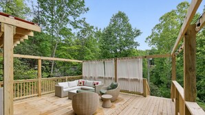 A wooden deck with outdoor furniture, including a sofa and chairs, surrounded by trees.