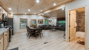 A spacious living area with a dining table, sofas, and a kitchen with wooden cabinets and a refrigerator.