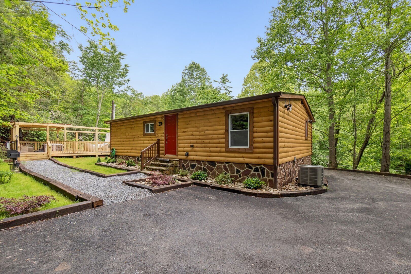 A log cabin with a red door, a stone foundation, and a wooden deck.