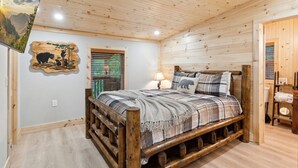 A wooden cabin bedroom with a bed, a nightstand, a lamp, and a wall-mounted artwork.