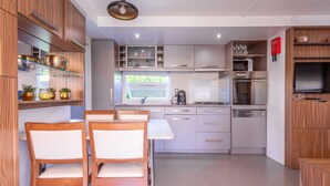 A modern kitchen with wooden cabinets, a dining table with chairs, and built-in appliances.