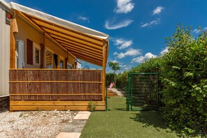 Un espace extérieur abrité, doté d’une terrasse en bois, d’un portail vert et d’une pelouse.