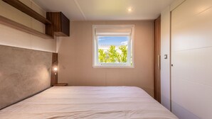 A bedroom with a bed, a window with a view of greenery, and a wooden headboard.