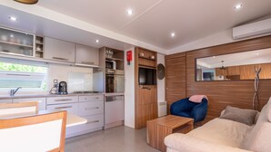 A modern kitchen with white cabinets, a dining area with a wooden table and chairs, a sofa, and a large mirror.