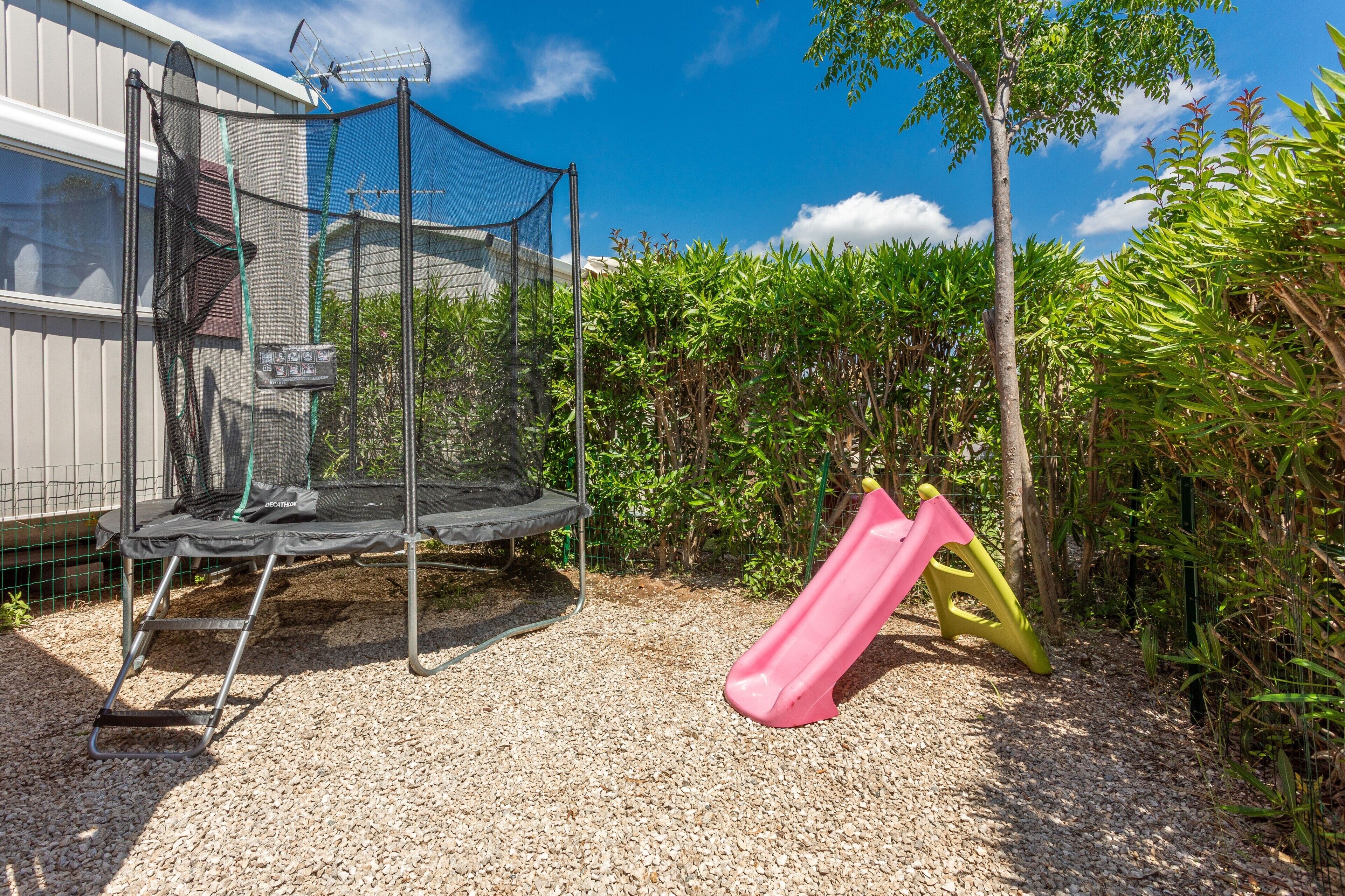 A trampoline, a slide, and a fenced area with dense foliage.