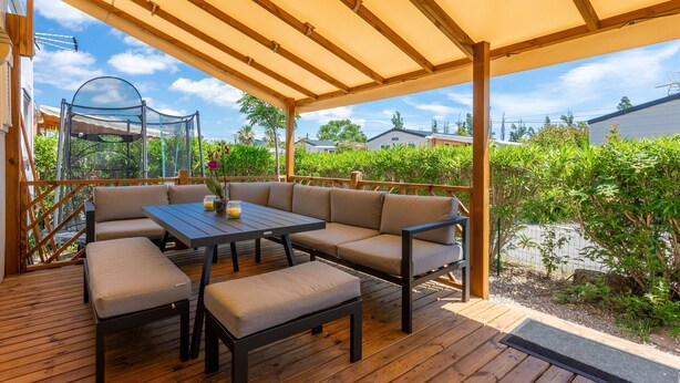 A covered outdoor seating area with a table and chairs, a glass enclosure, and a wooden deck.