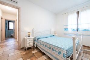 Un dormitorio con cama, mesitas de noche, una ventana con cortinas y un baño visible a través de una puerta abierta.